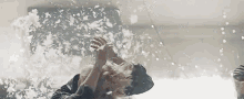 a person is laying on a bed with feathers falling on their head .