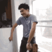 a man in a blue shirt is dancing in front of a window in a kitchen