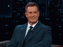 a man in a suit and tie sits with his hands folded