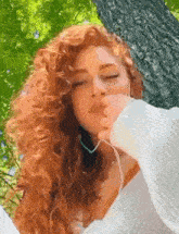 a woman with red curly hair is sitting in front of a tree .