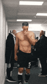 a shirtless soccer player with the number 5 on his shorts stands in a hallway