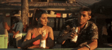 a man and a woman are sitting at a table with a bottle of corona beer