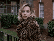 a woman wearing a leopard print coat is standing in front of a brick building