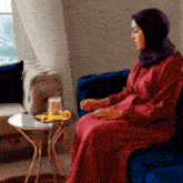 a woman in a red dress is sitting on a blue couch next to a table .