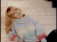 a girl in a sweater is laying down and says si maman