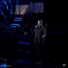 a man in a suit is pointing at the camera while holding a microphone