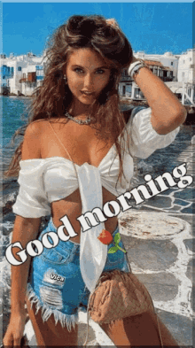 a woman in a white top and blue shorts is standing in front of a body of water and says good morning