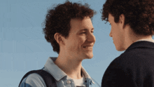 two young men with curly hair look at each other and smile