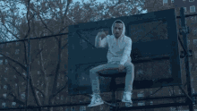 a man sitting on top of a basketball hoop giving a thumbs up