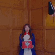 a woman is holding a gift box in front of a stack of gifts
