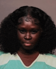 a woman with long curly hair is wearing a green and white striped shirt and looking at the camera .