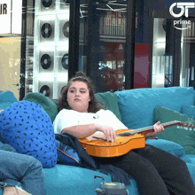 a woman sits on a blue couch playing a guitar with a prime logo in the background