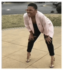 a woman in a pink jacket and black pants is kneeling on the sidewalk .