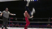 a man is doing a handstand in a wrestling ring while a referee looks on
