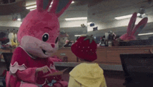 a pink bunny mascot is talking to a little girl in a strawberry hat