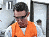 a man wearing safety glasses and an orange vest with the number 1 on it