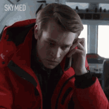 a man in a red jacket talking on a cell phone with skymed written on the bottom right