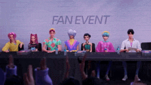 a group of people sitting at a table in front of a fan event banner