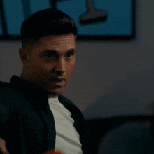 a man wearing a black jacket and a white shirt is sitting on a couch