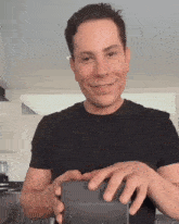 a man in a black shirt is smiling and holding a box
