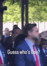 a man in a suit and tie is standing in a crowd and says guess who 's gay .