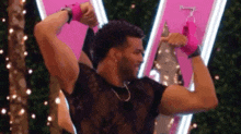 a man in a black shirt is flexing his muscles in front of a pink neon sign .
