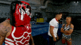 a wrestler in a red and white outfit is talking to a man and a woman in a room .