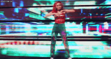 a woman in a red top and green pants is dancing on a stage in front of a large screen .