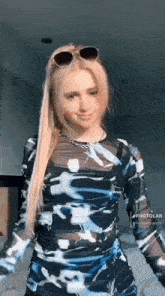 a woman wearing sunglasses and a blue and white dress is standing in a room .