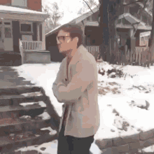 a man wearing glasses is standing in front of a snow covered house