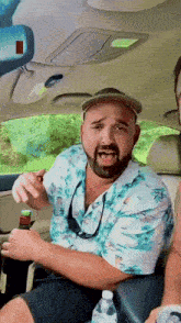 a man with a beard is sitting in a car with a bottle of water
