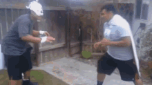 two men are standing next to each other in front of a house .