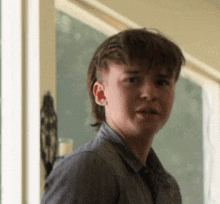 a young man with a mullet is standing in front of a window looking at the camera .