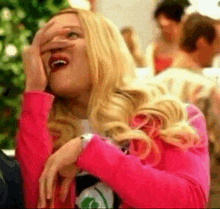 a woman in a pink jacket is covering her face with her hand while laughing .