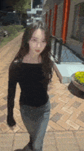 a woman in a black off the shoulder top and jeans is walking down a brick sidewalk .