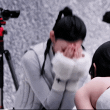 a woman is covering her face with her hands in front of a tripod