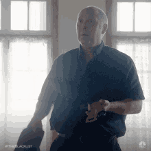 a man in a black shirt is holding a gun in front of a window with the hashtag #theblacklist on the bottom