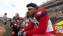 a group of football players are sitting on the sidelines of a football field .
