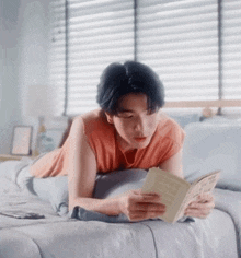 a young man is reading a book while laying on a bed .