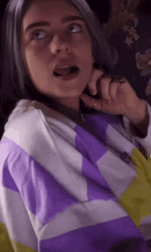 a girl with gray hair is talking on a cell phone while wearing a purple and yellow striped shirt .