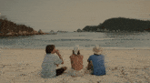 three people sitting on a beach looking at the water