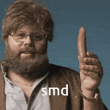 a man with glasses and a beard is holding up a sausage with smd written on the bottom right