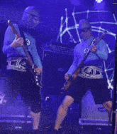 a man in a blue shirt with the letter a on it plays a guitar