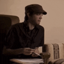 a man wearing a hat is sitting at a desk holding a pen .