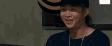 a man wearing a hat and a necklace is smiling and looking at the camera .