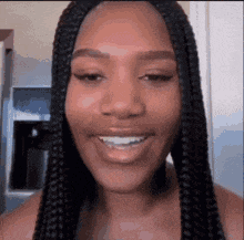a woman with braids is smiling for the camera in a kitchen .
