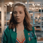 a woman in a green jacket and a striped top is looking at the camera .