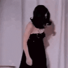 a woman in a strapless black dress is dancing in front of a window .