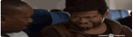 two men are sitting on a plane and one of them is wearing a hat and smiling