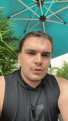 a man wearing a black tank top is standing under an umbrella